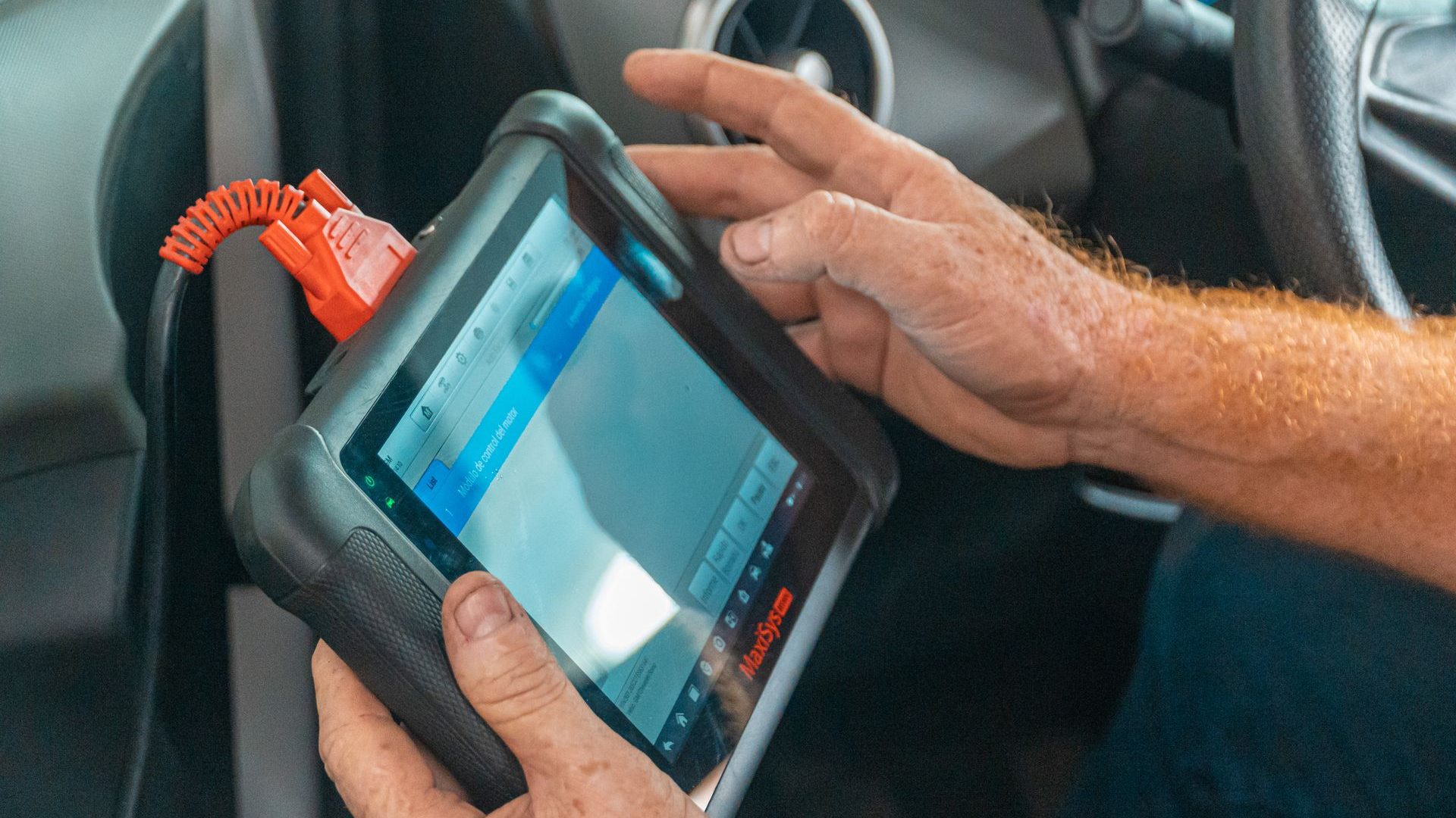 Hände halten ein Diagnosegerät mit Tablet-Display im Fahrzeuginnenraum