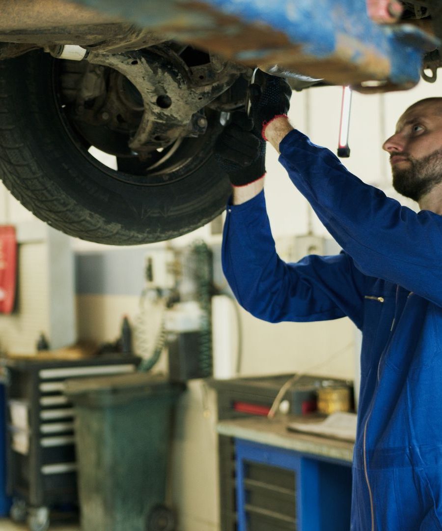 Mechaniker in blauem Overall arbeitet am Unterboden eines Fahrzeugs auf der Hebebühne